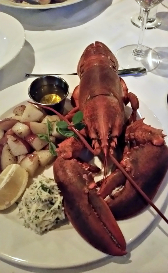 a boiled lobster on a plate next to potatoes and a wedge of lemon