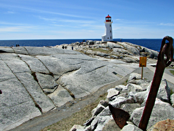 people walk over grey rocks toward a white lighthouse with a red top