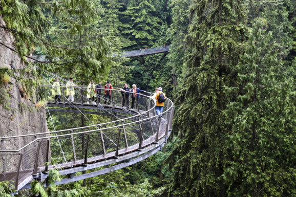 Visitors exploring the Capilano Cliff Walk through rainforest vegetation. It is a cantilevered and suspended walkways jutting out from the granite cliff face 230 metres above the Capilano River.