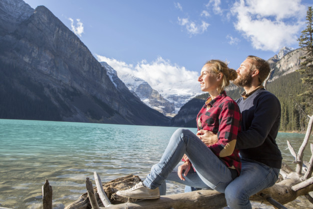 Young couple on a log tree by the lake, talking and enjoying the beautiful mountain lake scenery.