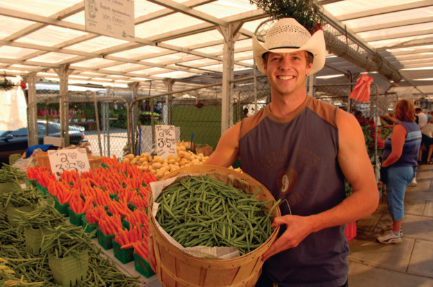 man holds a basket full of runner beans in a farmer's market