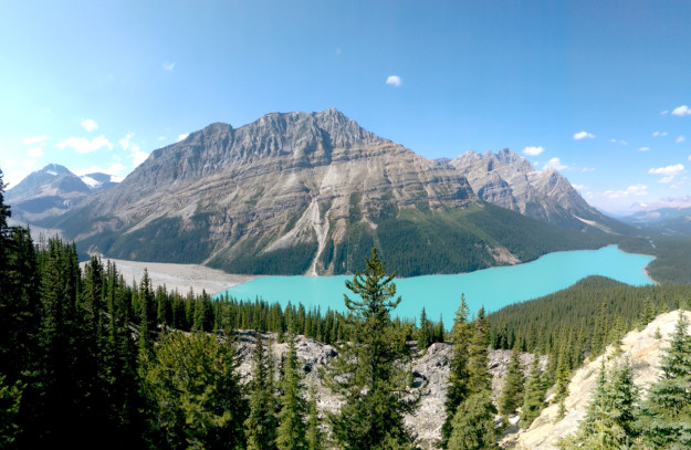 the turquoise water of Peyto lake sits at the bottom of a valley with a mountain in the background