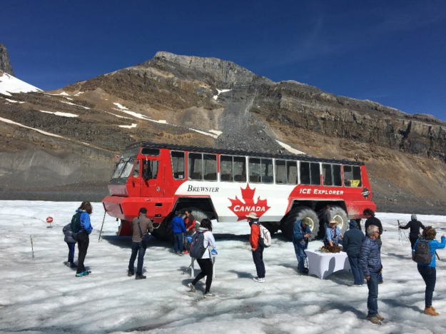 a tour group stand on the glacier in front of the offroad ice explorer tour bus