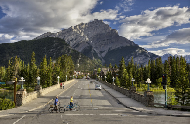 two children cycle across a road in front of the famous mountain peak in Banff