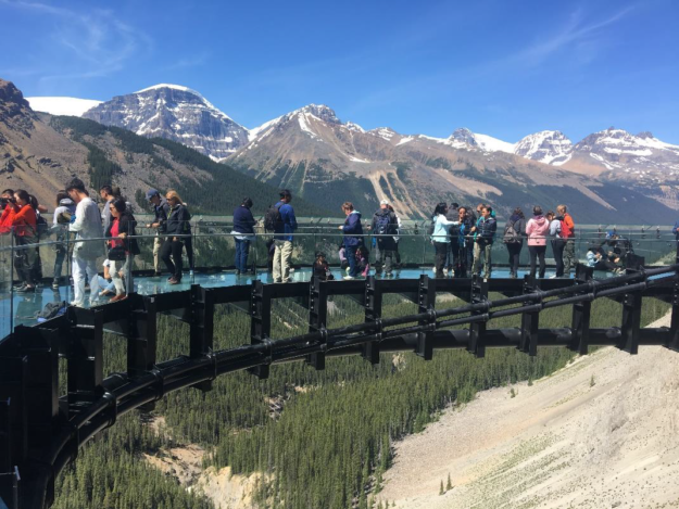 a tour group walks along a glass bridge suspended high above the valley floor