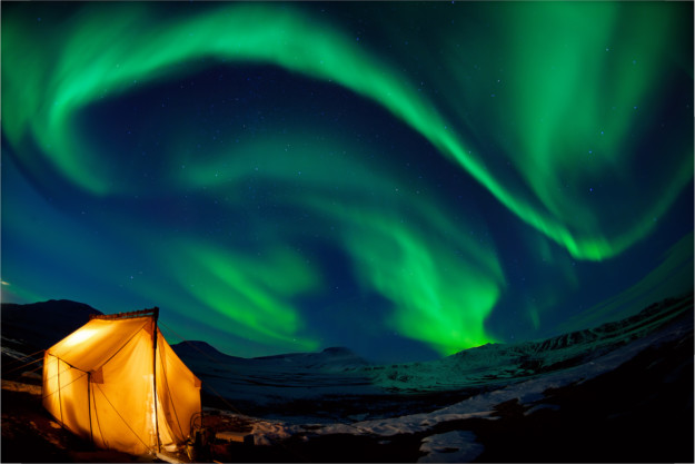 yellow tent standing beneath the green swirls of the northern lights