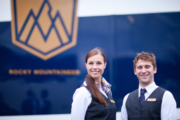 two Rocky Mountaineer staff smile in front of a train