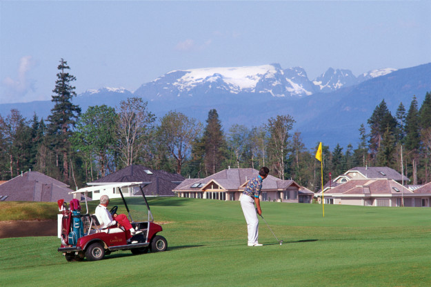 man putts on a golf course with a red golf buggy to his left and a snow-capped mountain in front