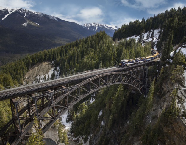 rocky mountaineer train crosses a steel bridge high above a deep valley