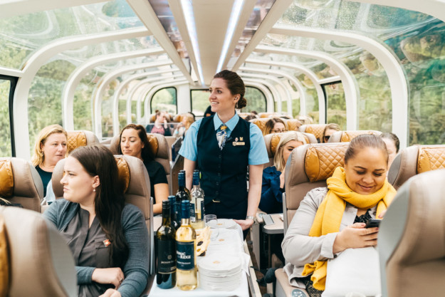 a drinks trolley is pushed through a train carriage with a glass ceiling and panoramic views