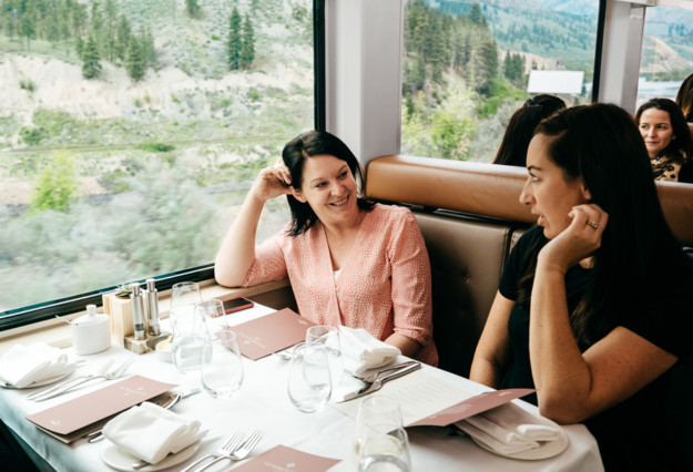 two women chat on a train with a view of the mountains out the window