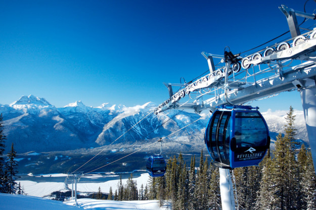 blue gondola reaches the top of a steep ski slope with mountains off in the distance