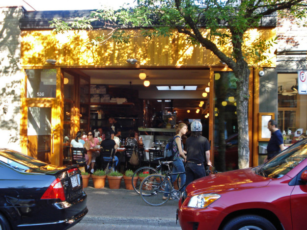 two men pushing bicycles walk past a busy bistro on a summer day