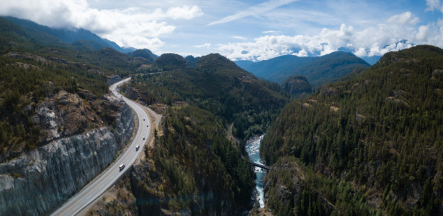 a highway curving past a rushing river in a dense green forest
