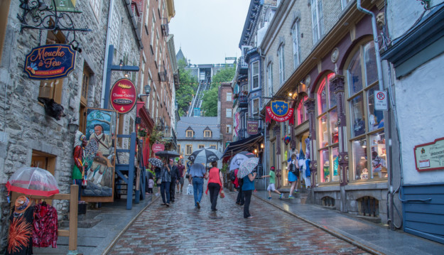people walk through the cobbled streets of old quebec sheltered under umbrellas