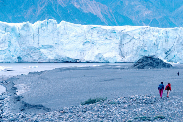 two people walk toward a giant glacier ice shelf