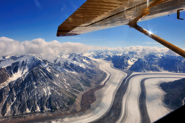 the edge of a small plane wing as it flies over a glacier