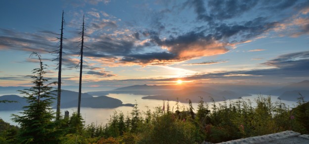the sun sets over the lakes and rolling hills of green forest