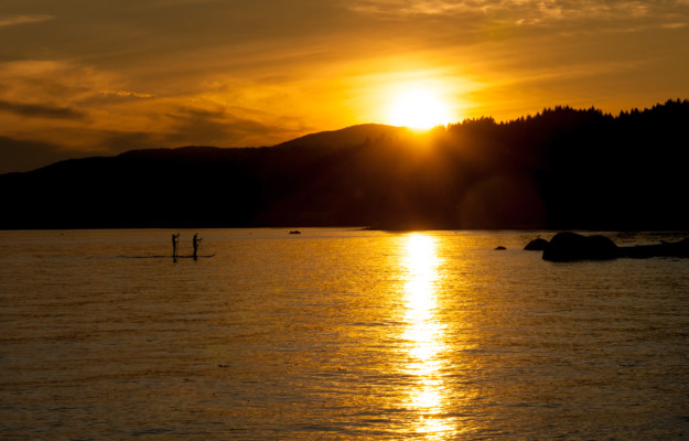 couple paddles board on a lake while the sun sets in the background