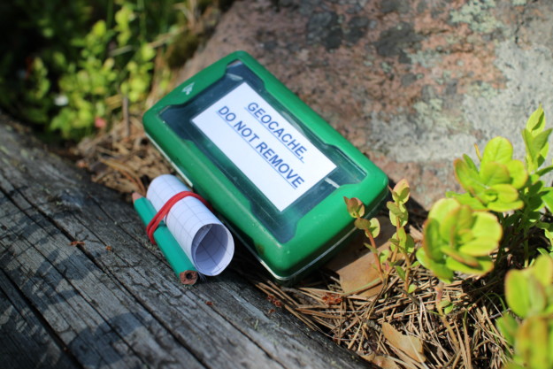a green box saying do not remove sits on a log next to a scroll of paper and a green pencil