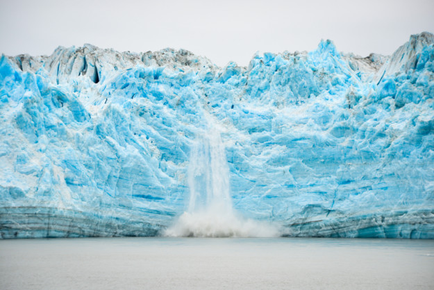 a giant waterfall pours off a bright blue glacier into the sea