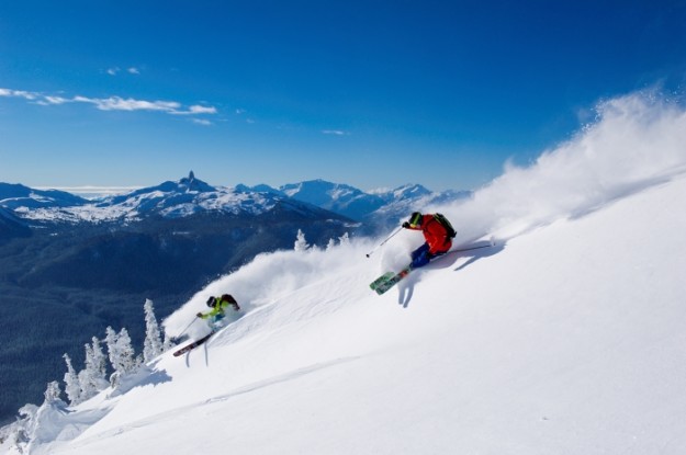 two skiers carving up the powder on a steep slope