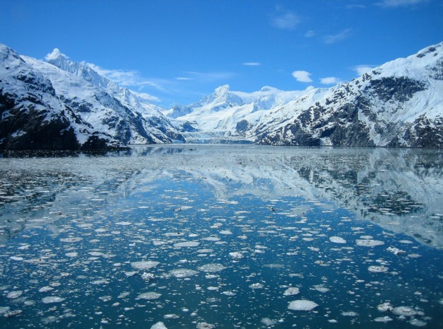 the ocean reflects a glacier and mountains in the background
