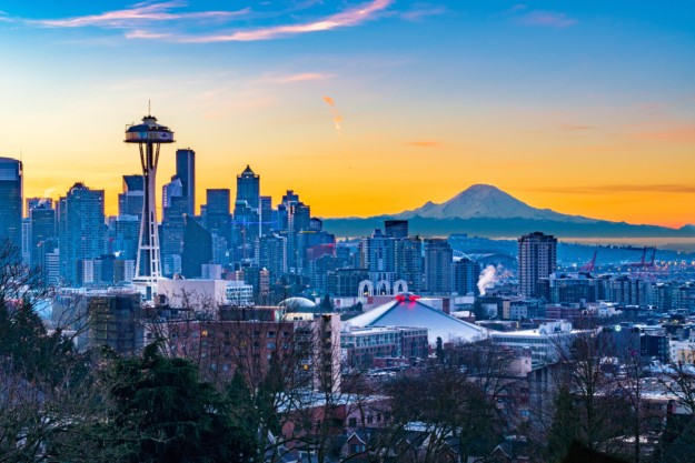 a brilliant orange and blue sky sits behind the seattle skyline with a mountain in the distance