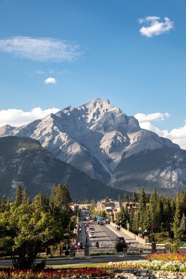 a giant picturesque mountain stands in the background above a busy road