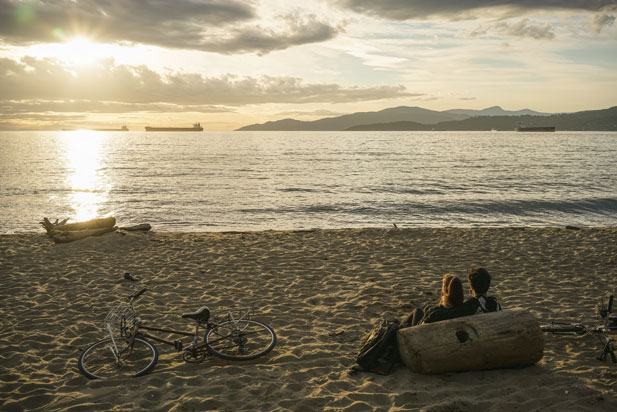 a couple sit on the beach looking out at the sunset over the English Bay, Vancouver