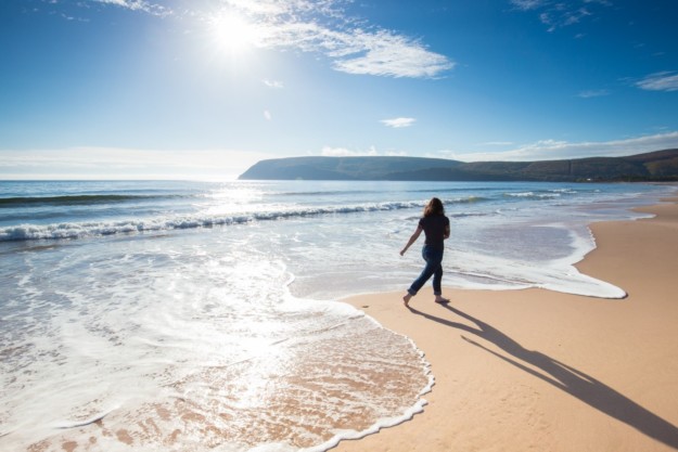 a woman skips along a beach with golden sand and bright blue water
