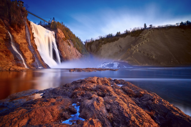 a large waterfall rushes down over red rocks