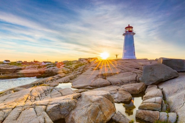 sun sets behind a white and red lighthouse on the rocks