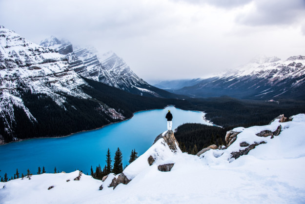 a man looks out over a crystal blue lake in a snowy landscape
