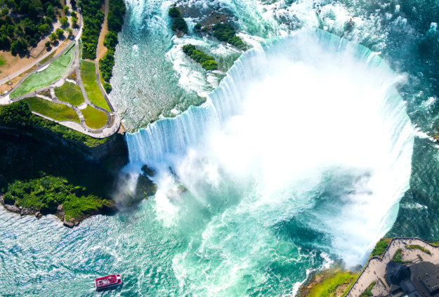 a boat tour approaches Niagara falls through turquoise and blue water