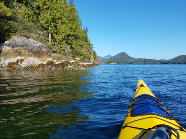 the front of a yellow kayak in a lake next to some rocks