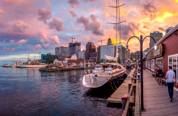 the sun sets on the waterfront in Halifax with a boardwalk and a yacht in the foreground