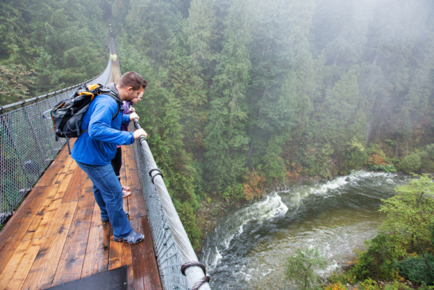 a couple look over the edge of the Capilano Suspension Bridge into the rushing water below