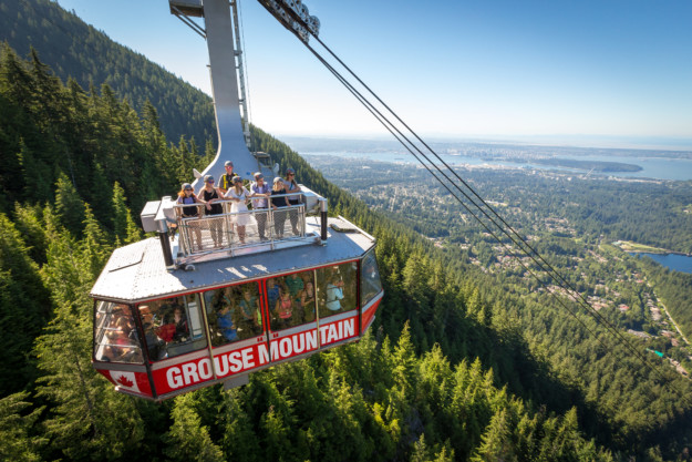 the Grouse Mountain gondola travels uphill full of people inside and a group standing on top