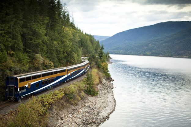 The Rocky Mountaineer train coming round a bend with a body of water to the right