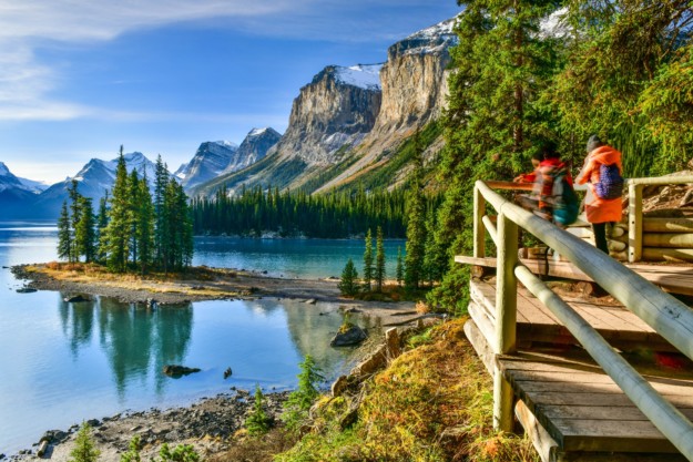 a couple of hikers look out over the blue waters of Maligne Lake with mountains in the background