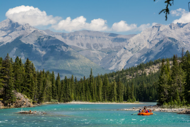 an inflatable orange raft paddles down a turquoise river