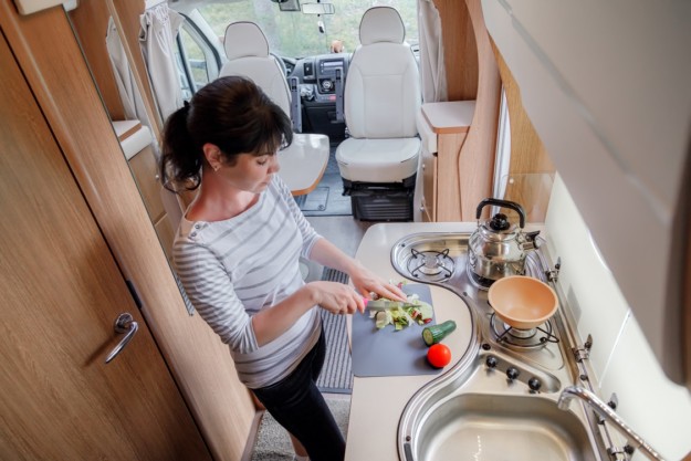A woman prepares food inside a motorhome's kitchen