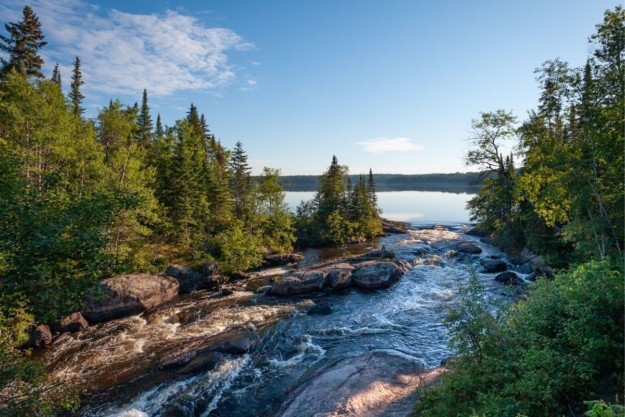 a rushing river feeds out to a lake between green trees