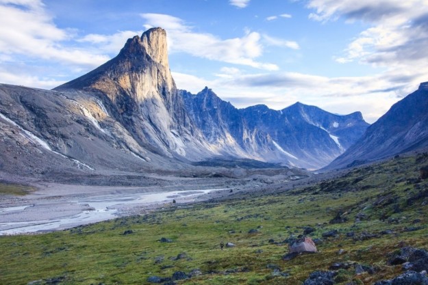 a huge mountain peak towers above a green valley