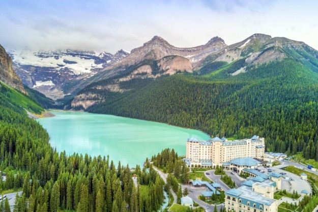 the turquoise water of Lake Louise stretches out between mountains with the Fairmont Hotel in the foreground