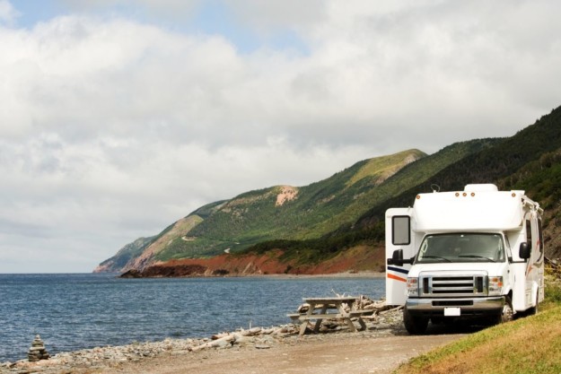 A motorhome vehicle parked with one door open beside a body of water