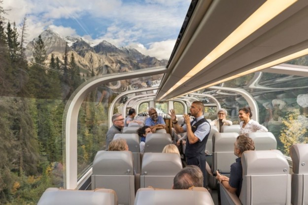 a rocky mountaineer guide speaks to passenger in the dome car of the train