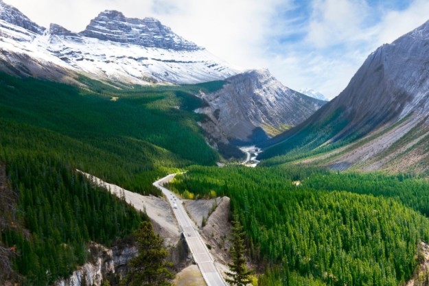a highway curves through the icefield parkway surrounded by trees and mountains