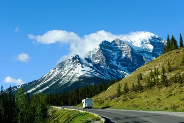 a motorhome drives along a road toward a snow-capped mountain
